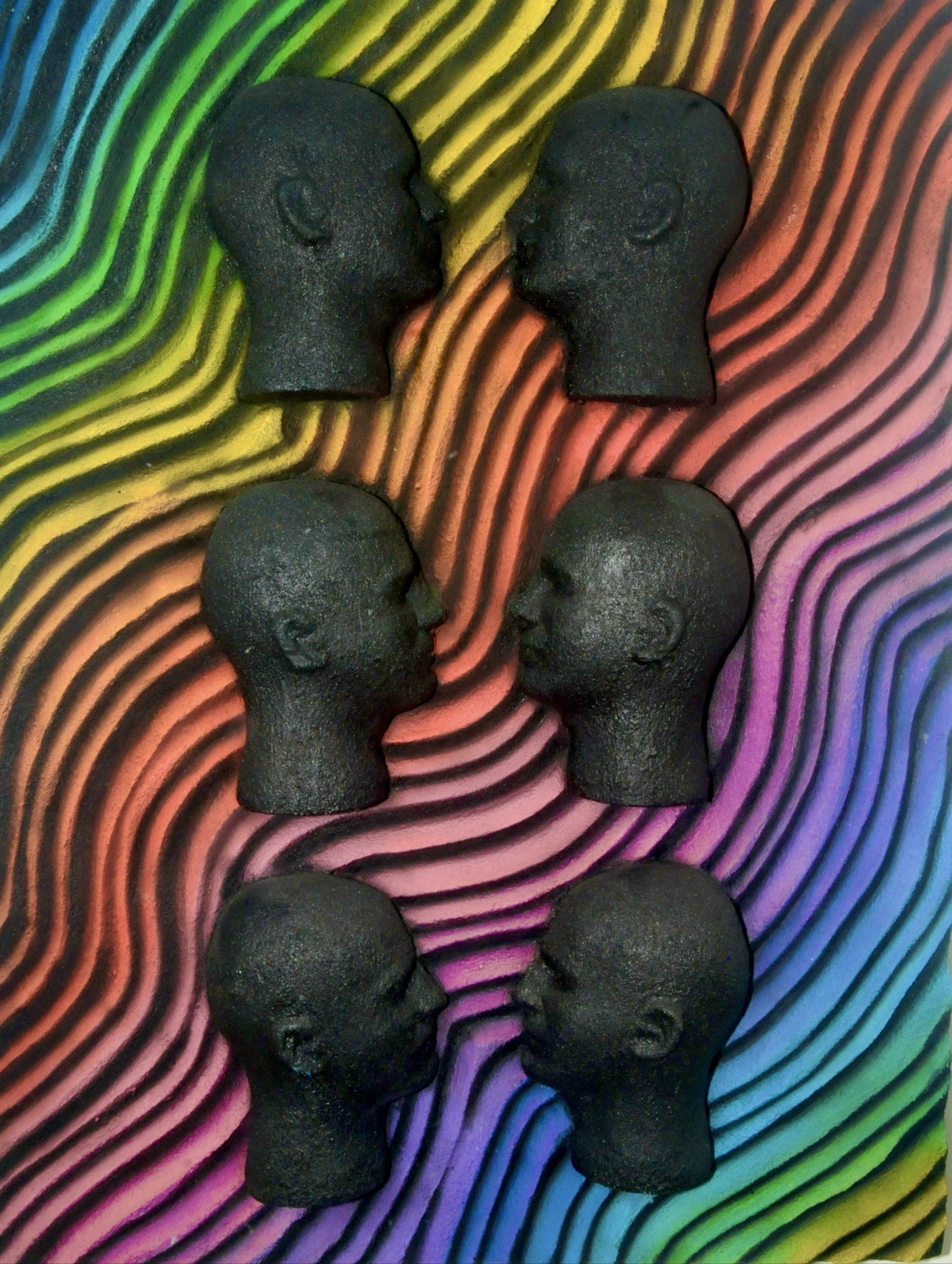 Face 2 Face, sculptural relief with six black faces in pairs over a rainbow-colored current