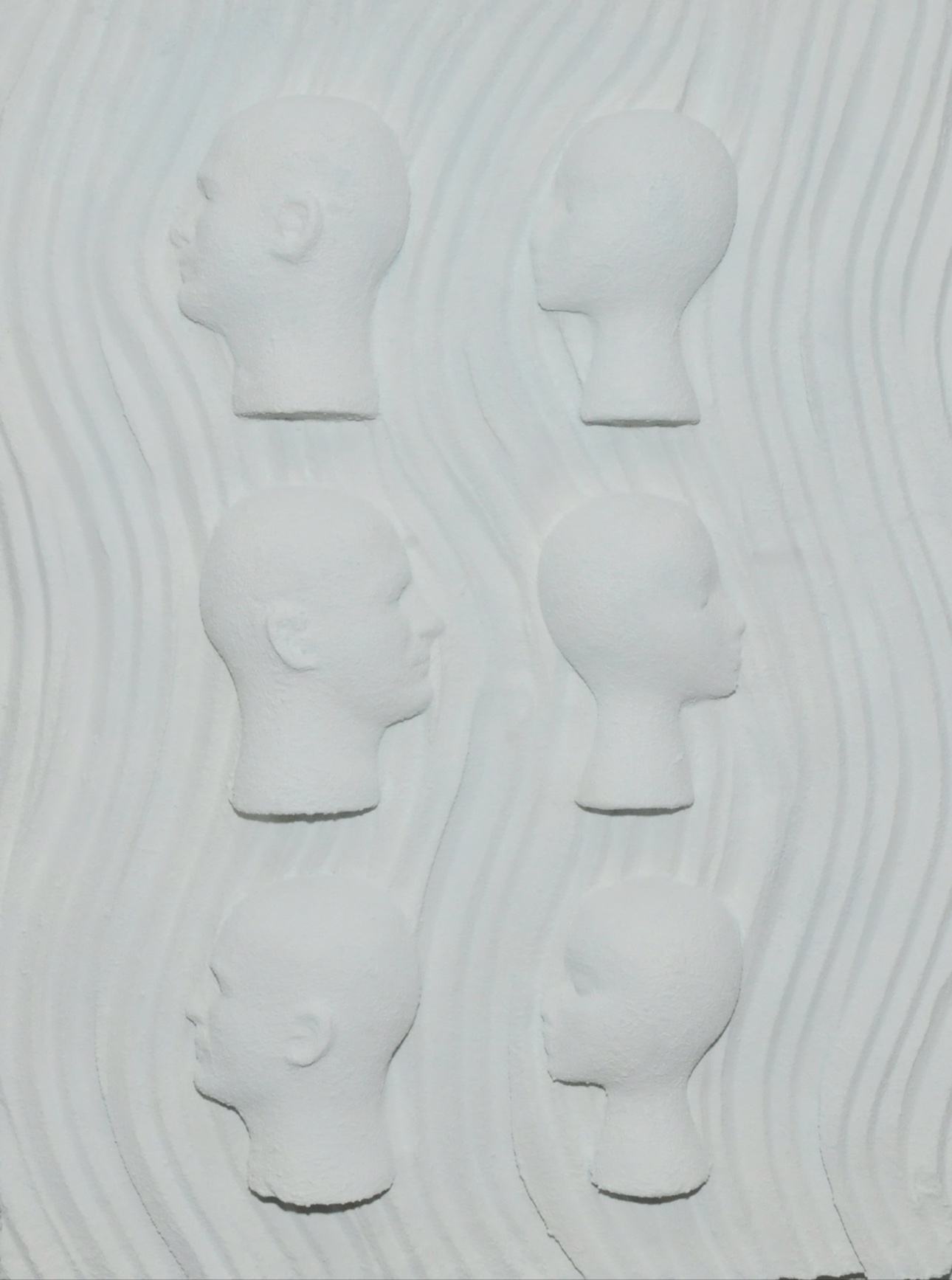 In the Same Light, sculptural relief with six pale faces in profile resting in carved white waves