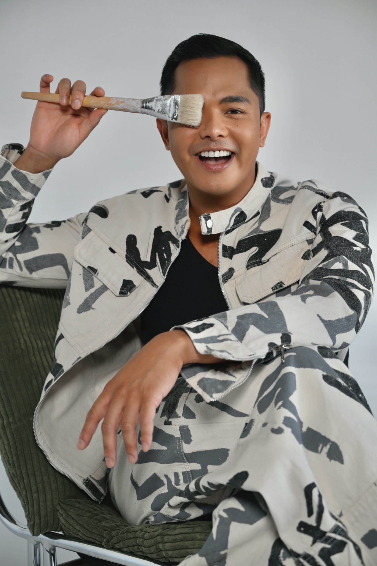 Playful portrait of Patrick holding a paintbrush across one eye