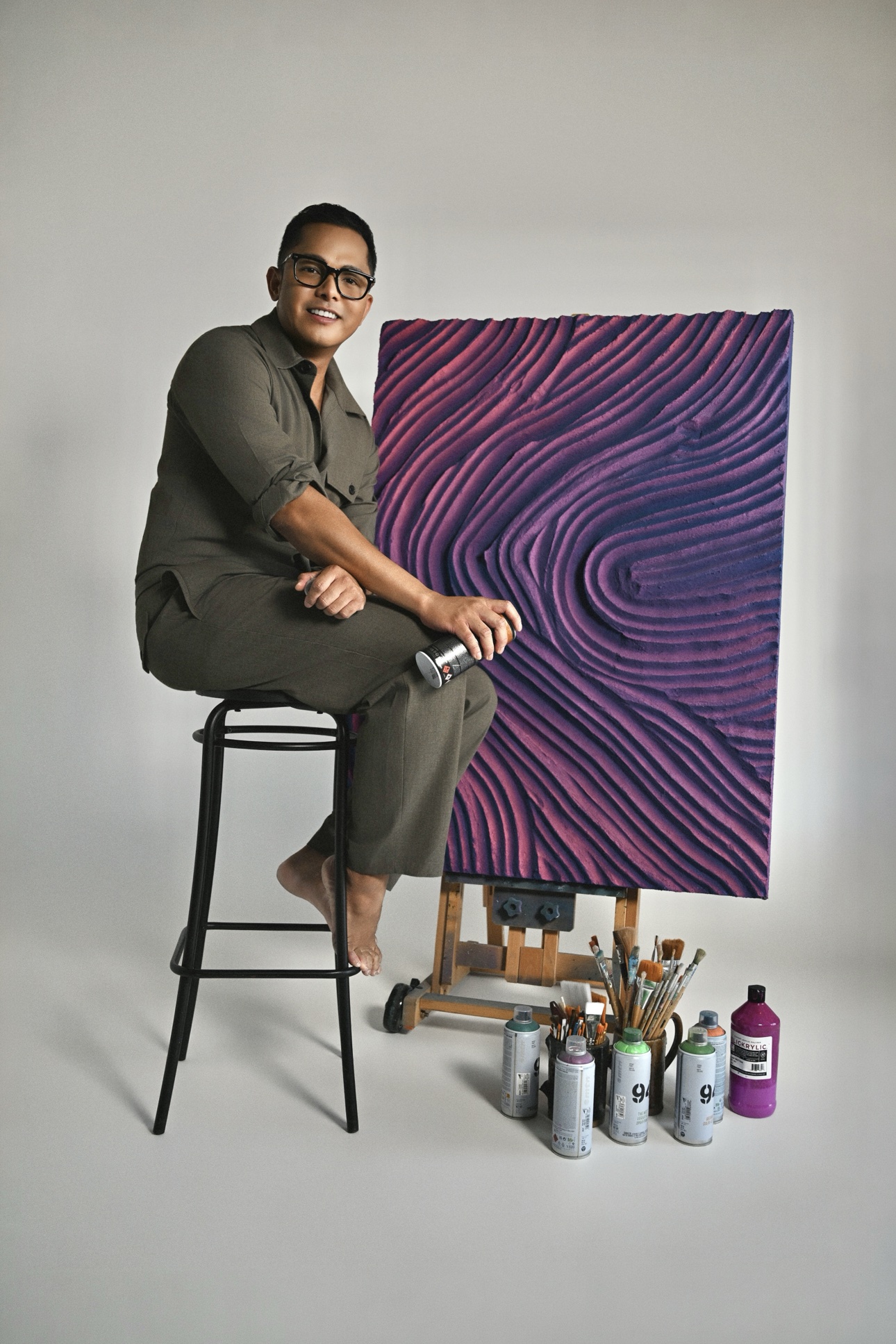 Patrick on a stool with a spray can, a purple relief panel on an easel beside him