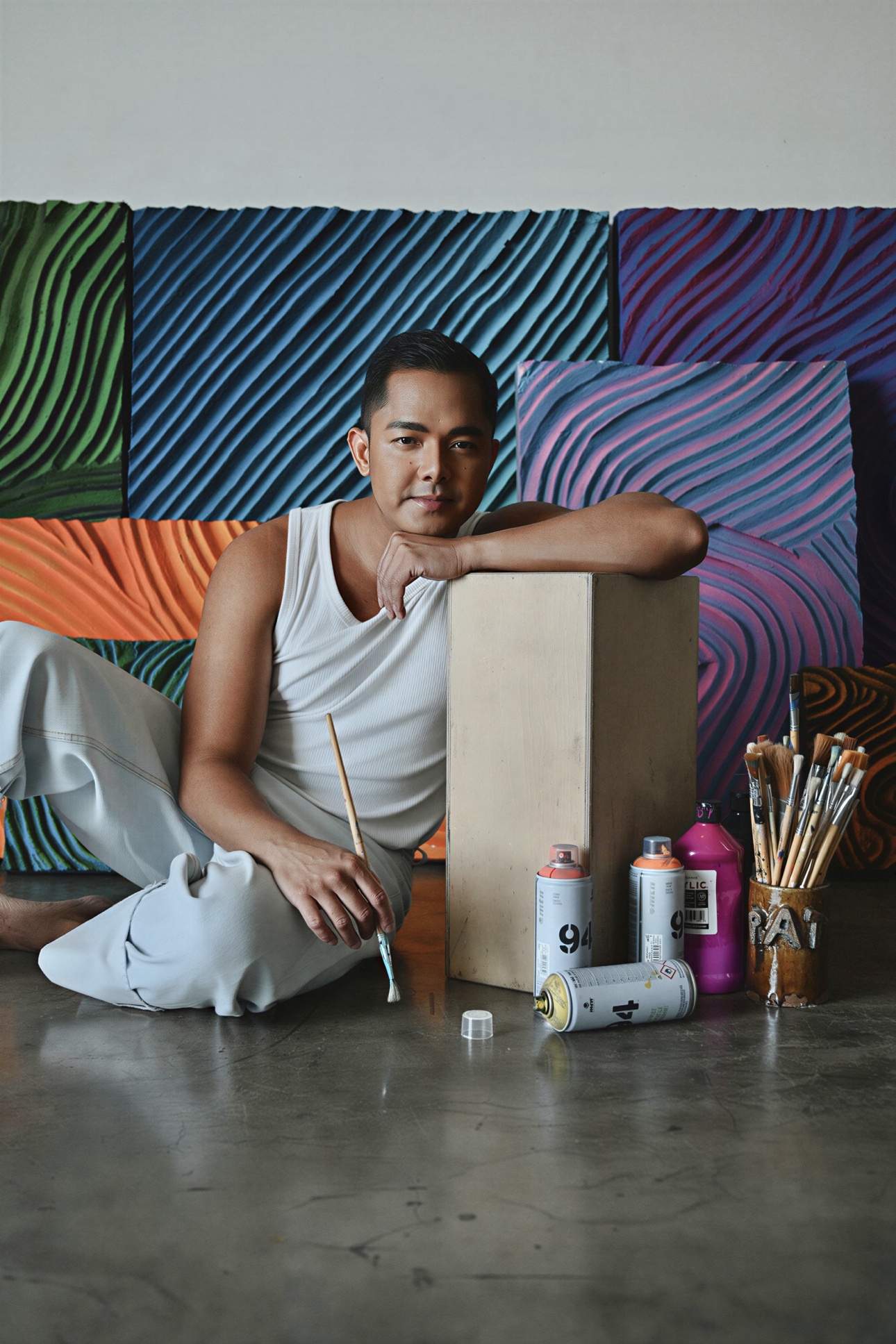 Patrick leaning on a wooden block with spray cans and brushes at his feet