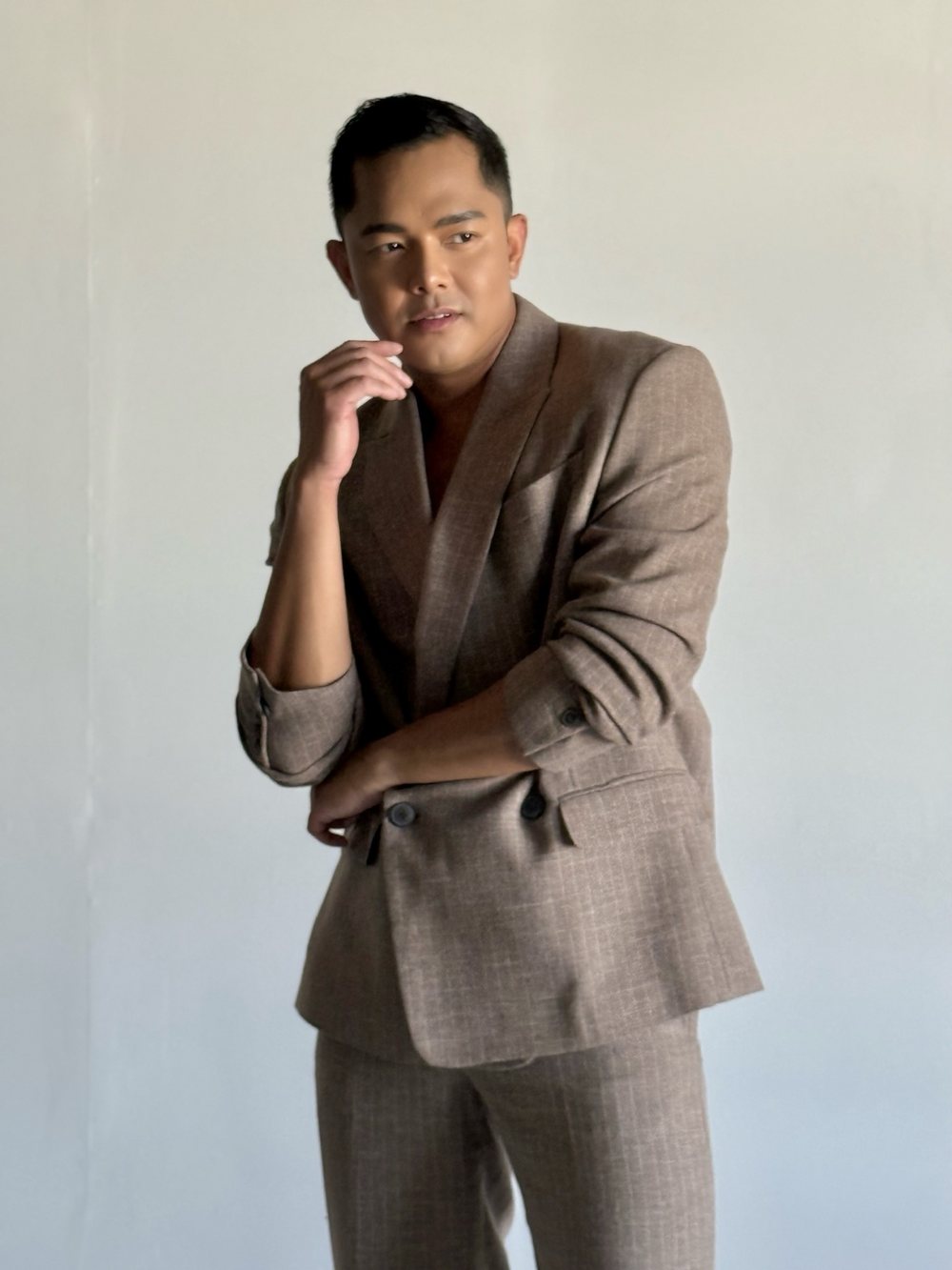 Patrick in a taupe suit, hand at his chin, colorful relief panels behind him
